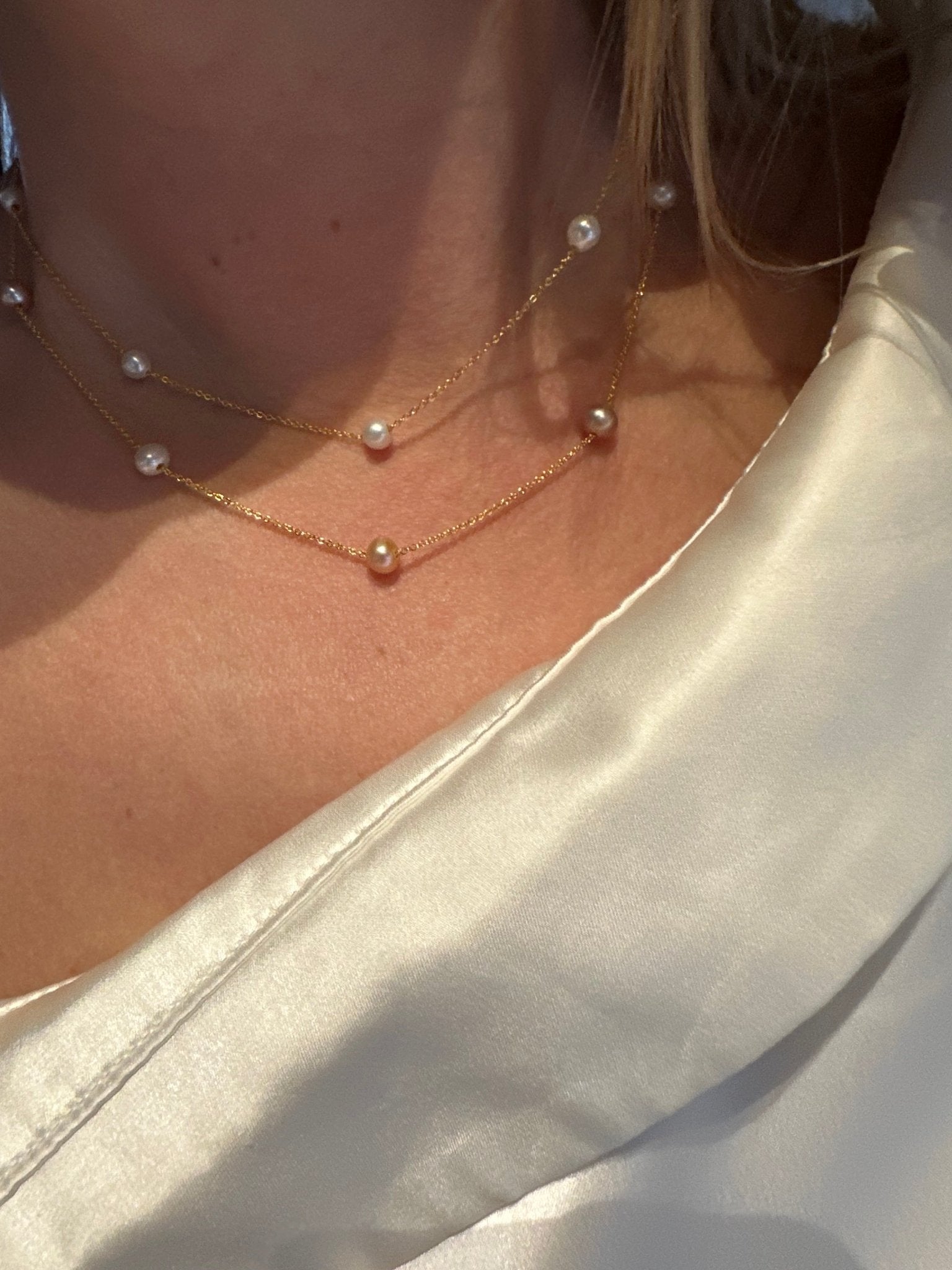 Anabela halskæde båret i lag med perler, closeup ved hals og kraveben